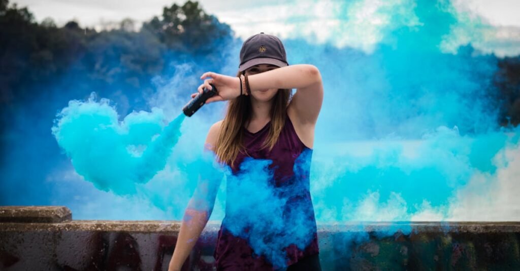 A stylish woman surrounded by bright blue smoke outdoors, creating a dynamic fashion statement.